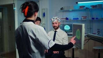 Medical doctor pointing on computer monitor with touch screen testing physical reactions and nervous system of man wearing brainwave scanning headset in technologically advanced laboratory video