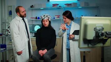 Team of medical researchers testing nervous system of woman patient, looking together at brain scan on computer monitor. Doctors examining evolution of treatment against diseases in equipped lab video