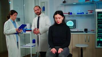 Team of scientists specializing in neurological medicine discussing health status of patient, brain functions, nervous system, tomography scan while woman waiting diagnosis of disease sitting in lab video