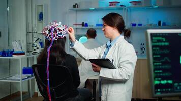 Back view of woman patient wearing performant brainwave scanning headset sitting in medical neurological laboratory while researcher adjusting it, examining nervous system typing on tablet. video