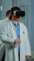 Vertical . Professional researcher wearing virtual reality glasses using medical inovation in lab analysing brain scan of patient. Team of neurological doctors working with equipment high tech simulator device video