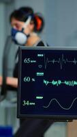 Vertical . Medical researcher examining EKG image showing on monitor while patinet with mask running on cross trainer testing heart rate using electrodes.Doctor monitoring physical endurance in science sport lab video