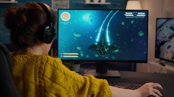 Pro gamer playing in the space shooter on personal computer. Woman gaming with teammates through headphones during online eSport tournament in action shot using technology network wireless video