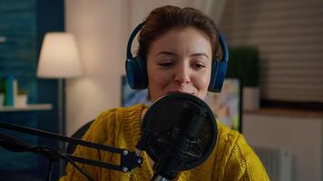 Famous woman arranging professional microphone and smiling while recording podcast for social media from home in night. On-air online production internet broadcast show host streaming live content video