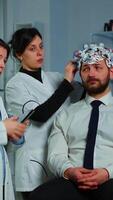 Vertical . Neurological researchers explaning treatment result pointing on monitor while medical scientist adjusting brainwave scanning headset preparing for brain scan analysing electrical activity video