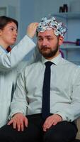 Vertical . Patient with brain scan discussing with researcher neurological doctor while adjusting brainwave scanning headset examining diagnosis of disease, explaning eeg results, health status, brain functions video