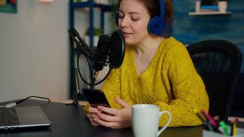 blogger reading questions from fans using smartphone during livestreaming from home podcast studio. Show production broadcast presenter streaming live content recording digital media video