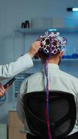Vertical . Man patient wearing performant eeg headset scanning brain electrical activity in neurological research laboratory while medical researcher controlling it, examining nervous system, nurse taking notes video