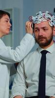 Vertical . Patient with brainwave scanning headset sitting in brain study laboratory while neurologist scientist adjusting high tech device. Man visiting professional doctor treating nervous system dysfunctions video