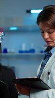 Vertical . Woman patient wearing performant eeg headset scanning brain electrical activity in neurological research laboratory while medical researcher adjusting it, examining nervous system typing on tablet. video