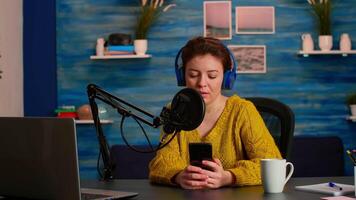Blogger woman recording for her blog in home studio reading messages on smartphone. On-air online production internet broadcast show host streaming live content for social media video
