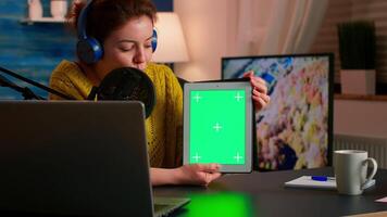 Influencer holding tablet with green screen and speaking into microphone during podcast in home studio. On-air production internet broadcast host streaming live content using chroma key mockup display video
