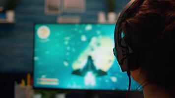 Over the shoulder pro gamer woman playing computer FPS shooter game on championship, talking into headset . Cyber performing on powerful computer in stylish room during gaming tournament video