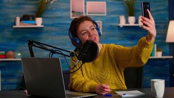 Social media influencer using phone for taking selfie recording podcast series for audience. On-air online production internet broadcast show host streaming live content for digital vlog video
