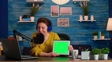Vlogger looking at laptop and talking about tablet with chroma key desktop. On-air production internet broadcast host streaming live content using mochup, green screen, izolated desktop video