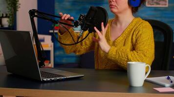 Podcaster recording online show at studio using headphones, microphone and laptop sitting in home podcast studio. On-air production internet broadcast show host streaming live content for social media video