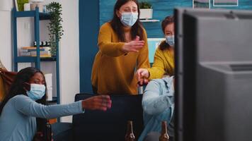 Mixed raced friends having fun playing game competion experiencing virtual reality keeping social distancing wearing masks to prevent sickness with covid. Diverse people in new normal party video
