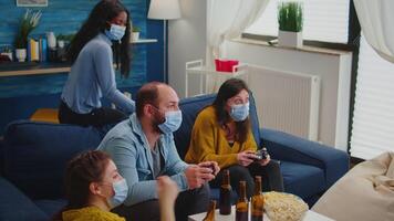 Sad friends because loosing playing games with wireless controller wearing face mask to prevent getting sick with corona in time of social pandemic. Group of people enjoying time together. video