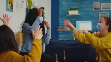 African woman with sticky note on forehead playing name game with happy friends wearing face mask to prevent infection with covid19 virus. Diverse group of people having fun at new normal party video