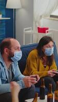 Vertical . Sad friends because loosing playing games with wireless controller wearing face mask to prevent getting sick with corona in time of social pandemic. Group of people enjoying time together. video