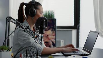 Podcast show host typing on laptop while talking to audience. Internet popular creative content creator chatting with public on live chat while speaking on modern microphone. video