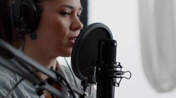 Young woman talking to audience while using professional microphone. Internet live radio talk show host presenting last news of day while sitting in studio with modern headphones on. video