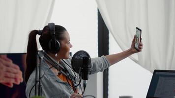 Popular social media influencer taking selfie photo with smartphone while streaming internet show. Creative content creator sitting in home studio while taking pictures with touchscreen mobile phone. video
