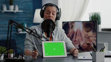 Influencer in studio promoting product on tablet with green screen display. Social media content creator recommending touchscreen device with chroma key with isolated background and mockup template video