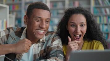 Happy African American man Arabian Latina woman using laptop computer technology device library high five project students learn task female male study educate enjoy connect internet knowledge clever video