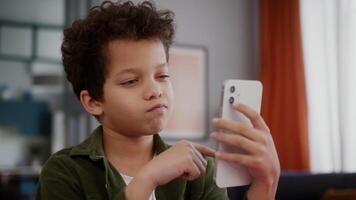 Boring little African American multiethnic boy son kid child at home using mobile phone scrolling bored screen smartphone social media disinterest app website gadget addict device internet addiction video