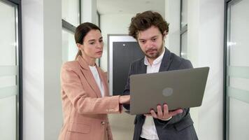 Two business people using a laptop together in a meeting. Happy business people looking at a slide presentation in an office. Presentation in boardroom with coworkers for corporate business seminar video