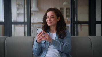 Caucasian woman girl female lady user at home couch sofa relaxing gadget addict social media internet addition using mobile phone chat smartphone browsing smiling happy order shopping cellphone app video