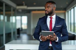 photo of man in navy suit outfit and red tie holding tablet in the office,