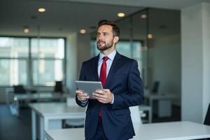 photo of man in navy suit outfit and red tie holding tablet in the office,