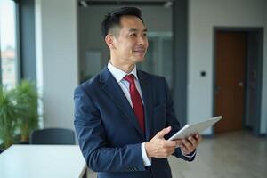 photo of man in navy suit outfit and red tie holding tablet in the office,