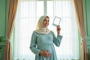 photo of muslim pregnant woman with hijab happy standing holding empty white photograph frame,