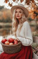 Blonde woman wearing a red skirt and white sweater holds a basket of apples in autumn park photo