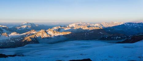 dawn panoramic view of the high mountains above the clouds from the glacier on the slope of Mount Elbrus photo