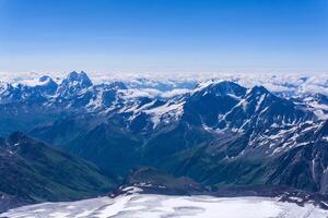 view of the high mountains above the clouds from the snowfield on the slope of Mount Elbrus photo