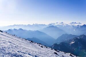 view from highland snowy slope to misty mountains in the rays of dawn photo