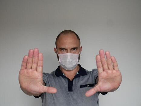 Stern looking man in medical mask shows open palm stop gesture on light background with copy space photo
