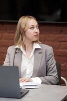 young woman sits at a table in front of a screen and and looks carefully to the side photo
