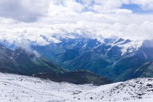 view of the Caucasus Mountains in the clouds from the slope of Mount Elbrus above the snow line photo