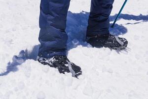 feet of an climber standing on a mountain glacier, wearing mountaineering boots equipped with crampons photo