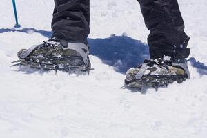 feet of an climber standing on a mountain glacier, wearing mountaineering boots equipped with crampons photo
