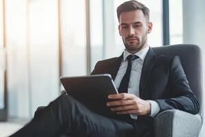 Close up of young businessman using digital tablet while sitting at his working place in office. Businessman using digital tablet photo