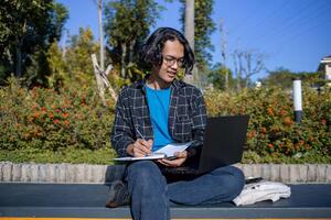 Male student sitting with laptop and books in campus garden. Working anywhere. Smiling photo