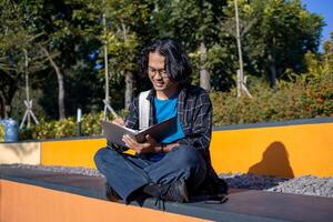 A male student is sitting in the park and writing on a book. photo