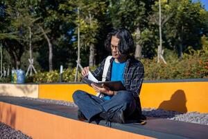 A male student is sitting in the park and reading a book. photo