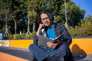 A male student is sitting in the park and reading a book. photo